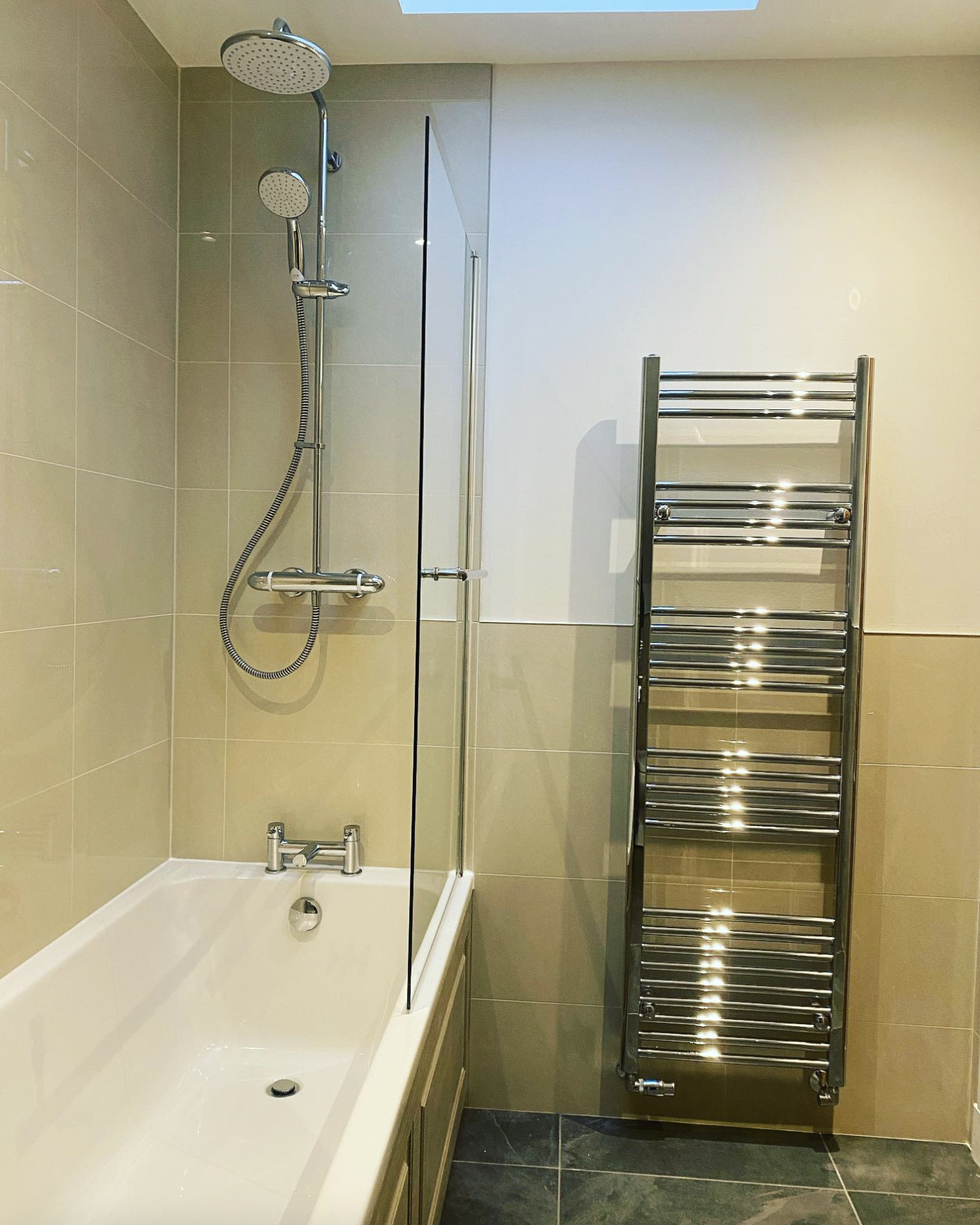 Bathroom with beige tiles, bath, shower and chrome heated towel rail