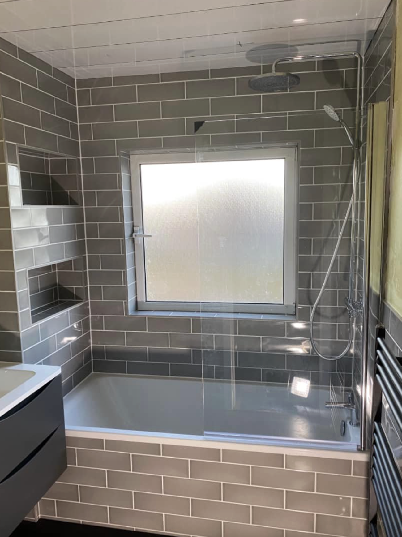 Bathroom with grey tiled walls and shower over bath