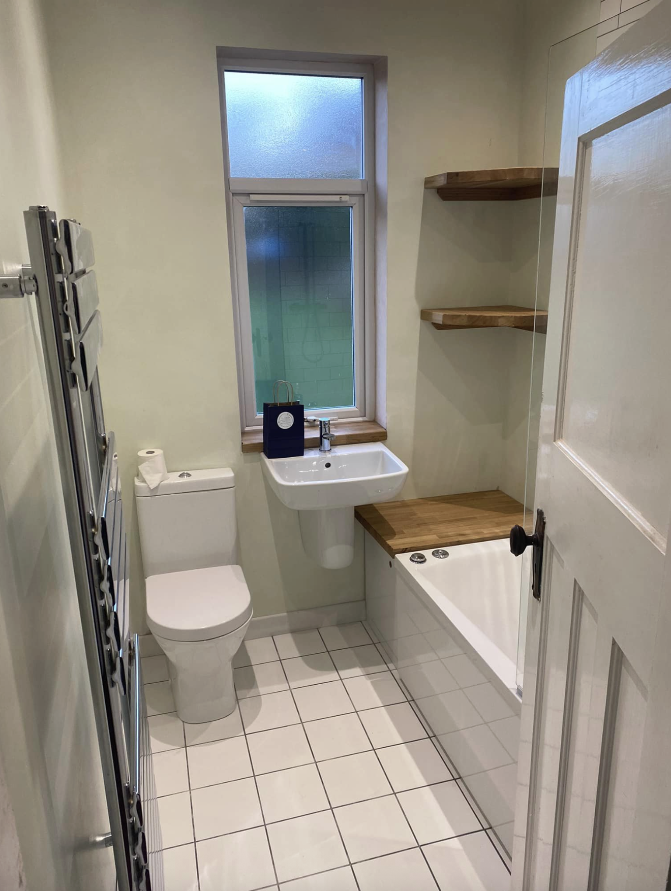 Bathroom with oak bath panel, floating oak shelves and chrome towel rail
