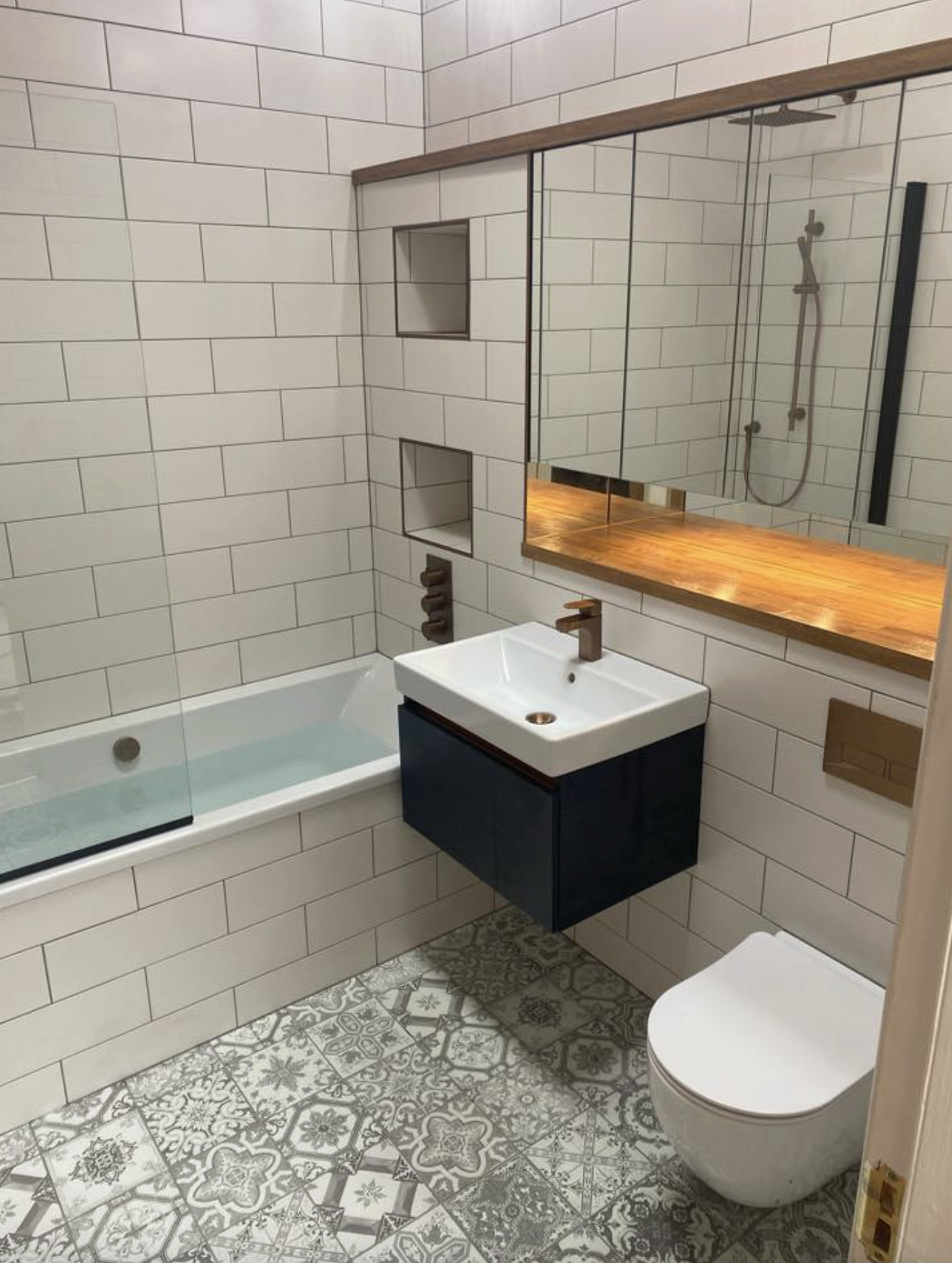 Modern bathroom with navy floating vanity, patterned floor tiles and oak shelf detail